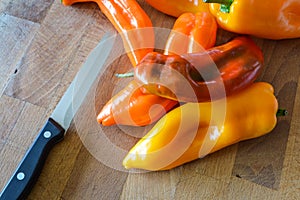 Group of sweet organic pointed peppers on a wooden cutting board with a kitchen knife