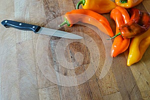 Group of sweet organic pointed peppers on a wooden cutting board with a kitchen knife