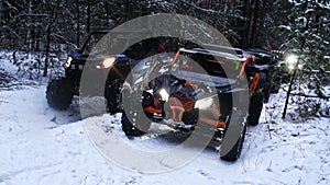 The group of sxs utv vehicles stands in the snow forest at dusk