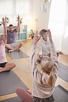 Group With Teacher Sitting On Exercise Mats Stretching In Yoga Class Inside Community Center