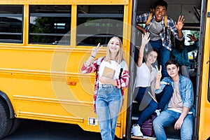 group of teen scholars sitting at school bus with driver inside and showing various gestures