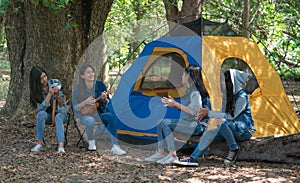 Group of teenage asian girls camping and resting at forest playing ukulele and take a photo happy together.
