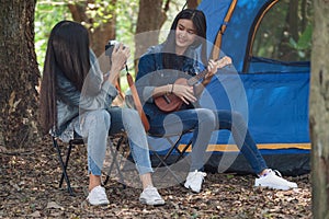 Group of teenage asian girls camping and resting at forest playing ukulele and take a photo happy together.