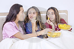 Group of teenage girls chatting and eating in bed