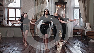 A group of teenage girls disperse to the sides of the row behind their teacher and begin to dance in the studio