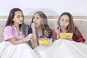 Group of teenage girls eating chips in bed