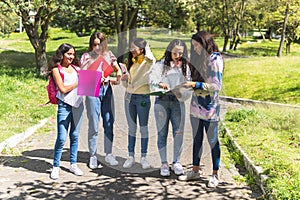 Group of teenage Latina student friends with their backpacks and notebooks reviewing their homework outdoors