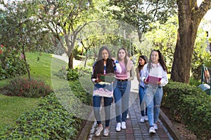A group of teenage Latinx friends walk with their backpacks on a path on their way to class photo