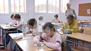 Group of teenage students working at class, listening explanations of teacher in classroom