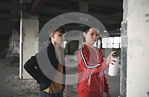 Group of teenagers boy gang indoors in abandoned building, using spray paint on wall.