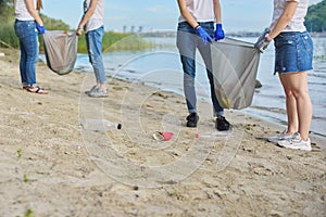 Group of teenagers on riverbank picking up plastic trash in bags