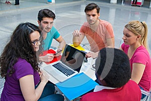 A group of teenagers sitting at the table in cafe, using laptop and drinking orange juice.