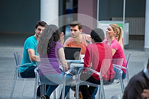 A group of teenagers sitting at the table in cafe, using laptop and drinking orange juice.