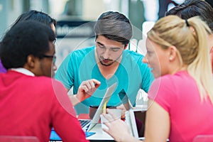 A group of teenagers sitting at the table in cafe, using laptop and drinking orange juice.