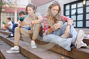 Group of teenagers smartphones sitting on stairs in school campus