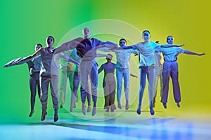 Group of teenagers, young dancers jumping together over green and yellow gradient background in neon light. Modern dance