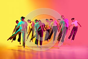 Group of teenagers, young dancers standing in a row and jumping up on pink and yellow background in neon light. Creative
