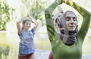 Group of teenages is engaged in fitness on pier by the lake or river. Young and positive girls go in for sports