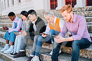 Group of teenegers browsing with the smartphones sitting together outdoors.