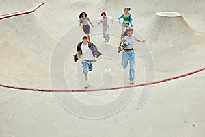 Group of teens in casual clothes, boy and girls running with skate on skateboard ramp. Activity and fun