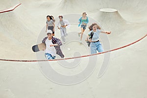 Group of teens in casual clothes, boy and girls running with skate on skateboard ramp. Activity and fun