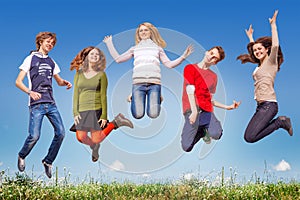 Group of teens jumping in the blue sky above the green grass