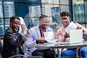 A group of their three successful African American businessmen in a stylish suit sit at the table and work with a laptop