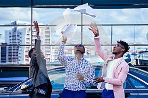 A group of their three successful African American businessmen in a stylish suit throw papers up against a skyscraper of