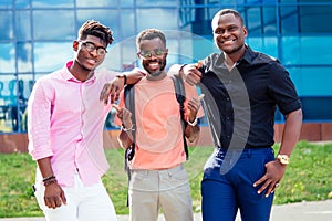 A group of three African Americans male friends in stylish clothes stand against the background of the blue windows of