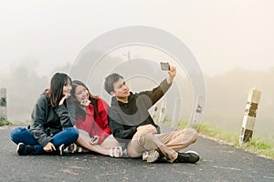 A group of three Asian friends wearing a sweater using a selfie phone to take pictures in a tourist attraction. Along the road