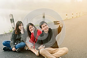 A group of three Asian friends wearing a sweater using a selfie phone to take pictures in a tourist attraction. Along the road