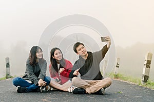 A group of three Asian friends wearing a sweater using a selfie phone to take pictures in a tourist attraction. Along the road