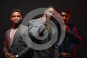 A group of three black men in stylish suits posing isolated in studio