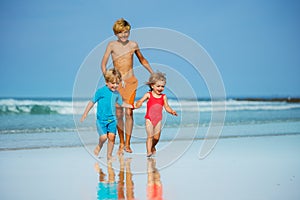 Group of three children run on sand beach holding hands