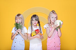 Group of three cute healthy school girls holding vegetables, lifestyle. Concept of healthy food for children. Proper balanced food