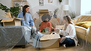 Group of three female happy friends unpacking, moving into student flat.