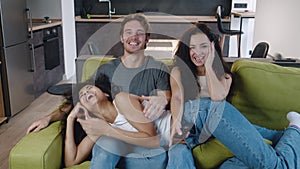 Group of three friends talking, laughing and watching TV together while sitting on the couch. Mixed race young people