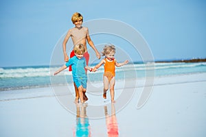 Group of three kids run on sand beach holding hands