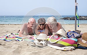 Group of three people friends mature and senior hugging enjoying together holidays at the beach having fun with smart phone -