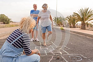 Group of three people like adults and senior - two seniors playing at hopscotch with a curly woman looking at the mature woman