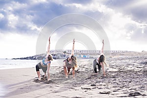 Group of three people women friends do exercises of balance and strenght like yoga and pilates on the beach. coast and sand scenic