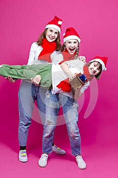 Group of Three Positive Caucasian Girls With Santa Hats Having Fun While Lifting Teenage Girl Holding Hands Closed Against Trendy