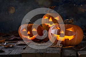 A group of three pumpkins and fallen dry leaves on wooden table.