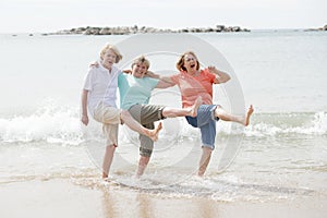 Group of three senior mature retired women on their 60s having fun enjoying together happy walking on the beach smiling playful