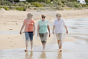 Group of three senior mature retired women on their 60s having fun enjoying together happy walking on the beach smiling playful