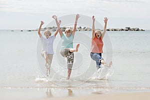 Group of three senior mature retired women on their 60s having fun enjoying together happy walking on the beach smiling playful