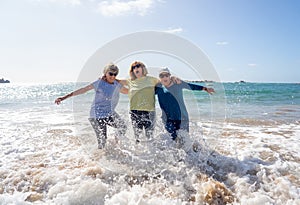 Group of three senior women laughing as falling down in the water on beach. Humor senior health