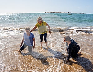Group of three senior women laughing as falling down in the water on beach. Humor senior health