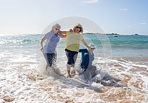 Group of three senior women laughing as falling down in the water on beach. Humor senior health