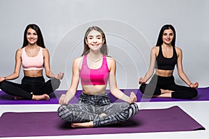 Group of three slim women sitting in lotus position on yoga mats and meditating with their hands on knees